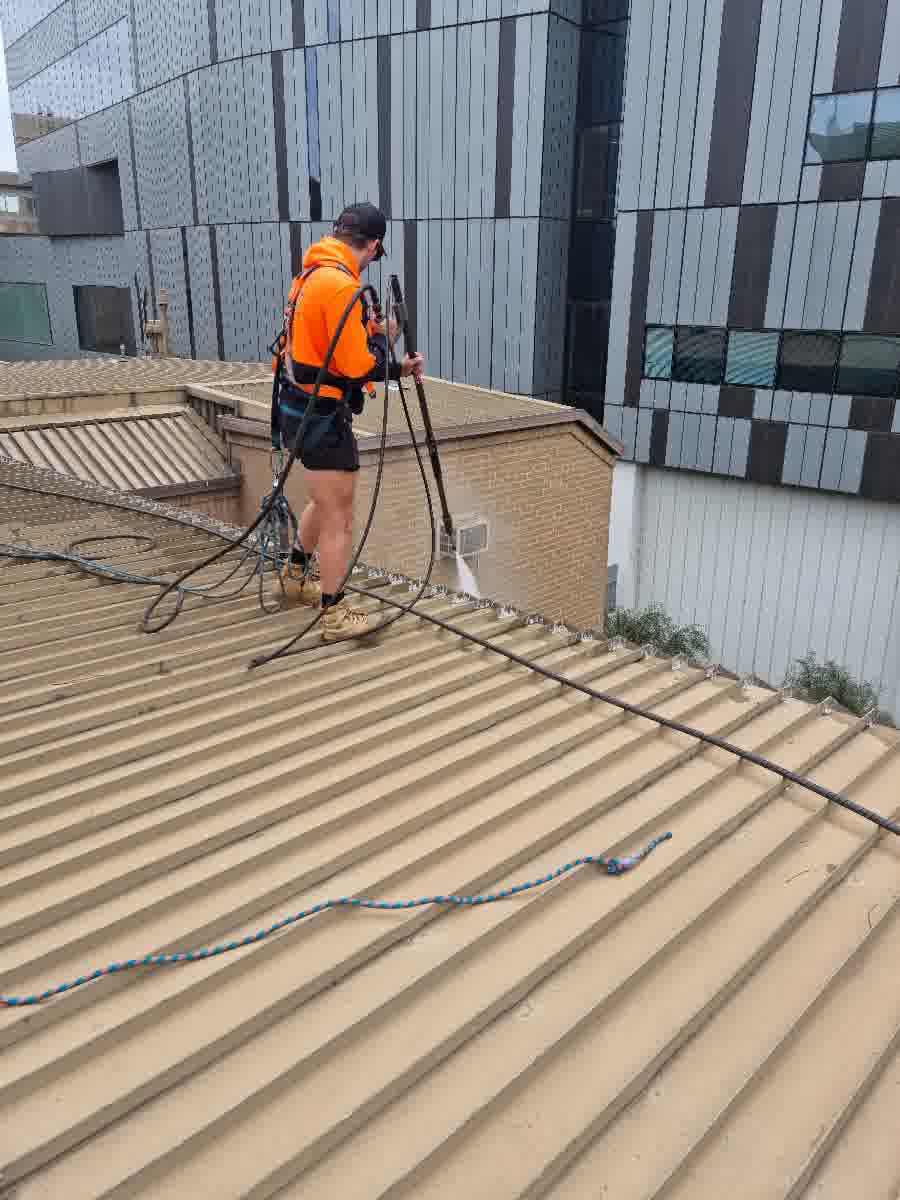 Technician pressure cleaning gutters on a commercial building roof